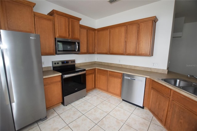 kitchen with appliances with stainless steel finishes, brown cabinetry, a sink, and light tile patterned flooring