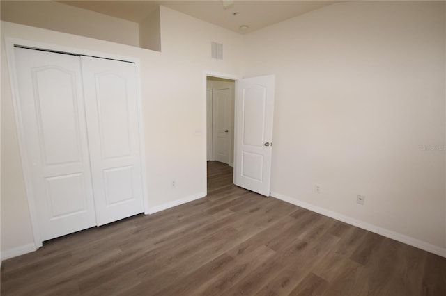 unfurnished bedroom featuring baseboards, wood finished floors, a closet, and high vaulted ceiling
