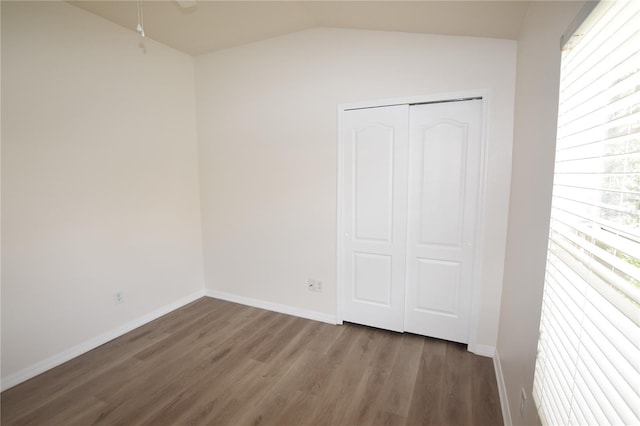empty room featuring lofted ceiling, wood finished floors, and baseboards