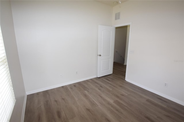 empty room with wood finished floors, baseboards, and a high ceiling