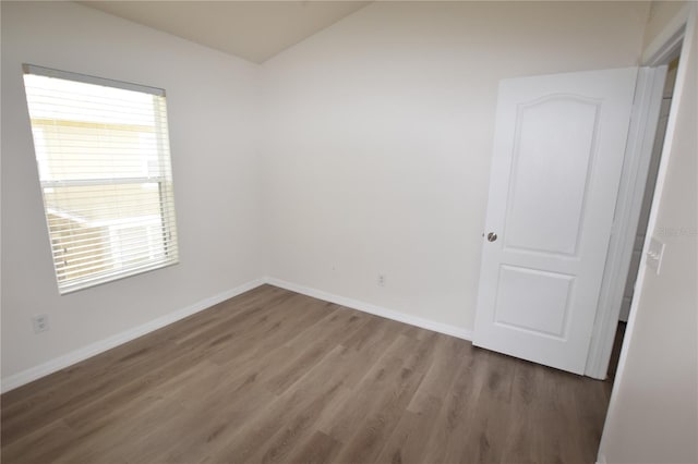spare room featuring wood finished floors, baseboards, and lofted ceiling