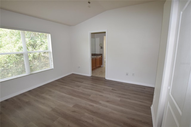 empty room featuring vaulted ceiling, wood finished floors, and baseboards