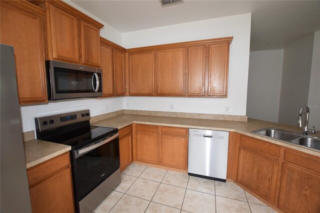 15349 Oak Apple Ct, Winter Garden, FL 34787 - kitchen with appliances with stainless steel finishes, a sink, light tile patterned floors, brown cabinetry, and light countertops