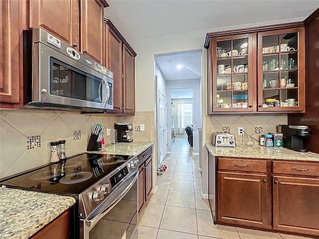 1027 Cedar Bay Ln, Winter Springs, FL 32708 - kitchen featuring stainless steel appliances, tasteful backsplash, light tile patterned floors, glass insert cabinets, and light stone counters
