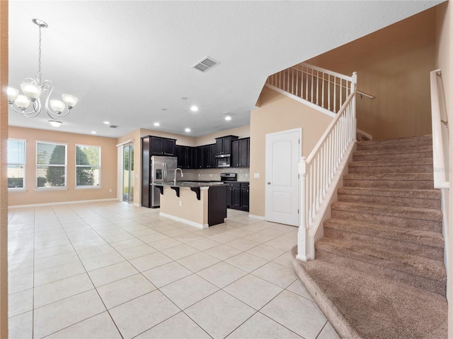 kitchen with light tile patterned floors, open floor plan, a kitchen bar, dark cabinets, and appliances with stainless steel finishes