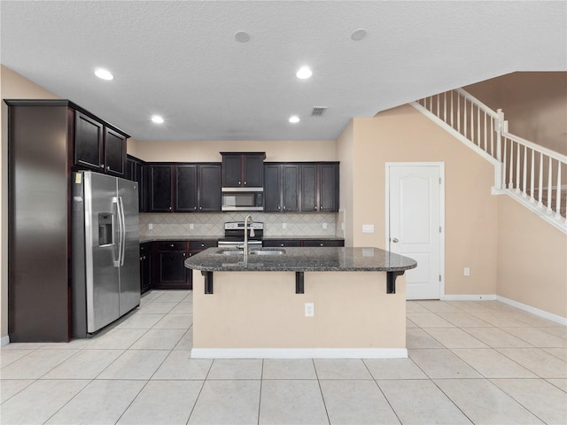 kitchen featuring appliances with stainless steel finishes, a sink, dark stone counters, backsplash, and light tile patterned floors