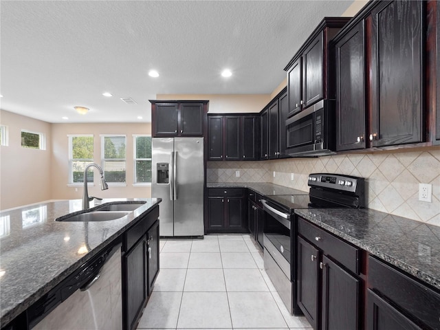 kitchen featuring appliances with stainless steel finishes, a sink, dark stone counters, backsplash, and recessed lighting