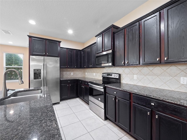 kitchen with appliances with stainless steel finishes, a sink, dark stone counters, tasteful backsplash, and light tile patterned floors