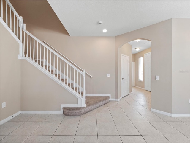 foyer featuring stairway, arched walkways, tile patterned floors, baseboards, and recessed lighting