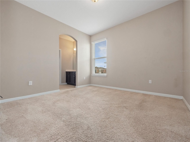 spare room featuring arched walkways, light carpet, and baseboards