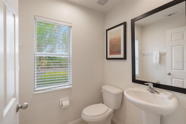 bathroom featuring baseboards, toilet, healthy amount of natural light, and a sink