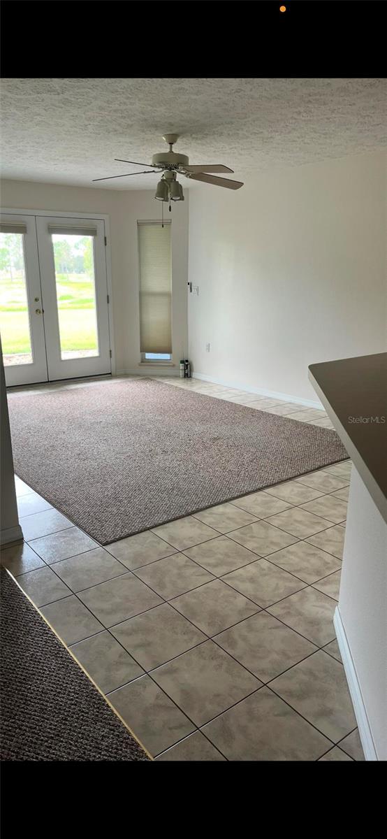 unfurnished room with a textured ceiling, light tile patterned flooring, a ceiling fan, and baseboards
