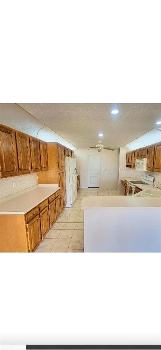 kitchen featuring white appliances, a peninsula, brown cabinets, light countertops, and recessed lighting