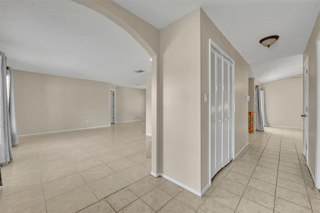 hallway with light tile patterned flooring, arched walkways, baseboards, and a textured ceiling