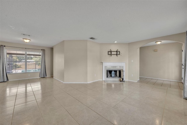 unfurnished living room featuring light tile patterned flooring, baseboards, a textured ceiling, and arched walkways