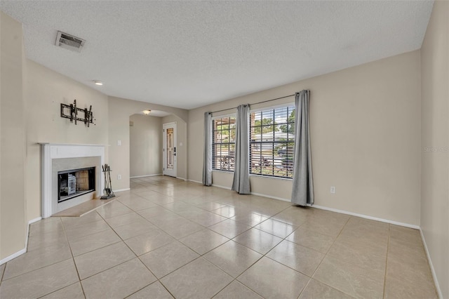 unfurnished living room featuring arched walkways, a textured ceiling, tile patterned flooring, a glass covered fireplace, and baseboards