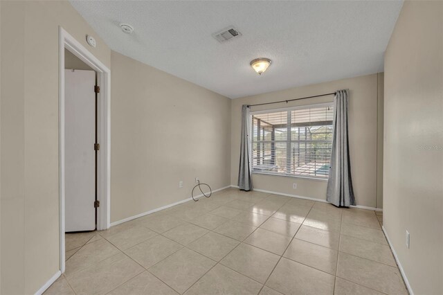 empty room featuring light tile patterned floors, a textured ceiling, baseboards, and a smoke detector