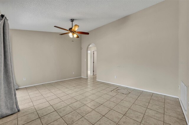 empty room featuring arched walkways, ceiling fan, light tile patterned floors, a textured ceiling, and baseboards