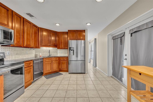 kitchen with appliances with stainless steel finishes, a sink, tasteful backsplash, light tile patterned floors, and recessed lighting