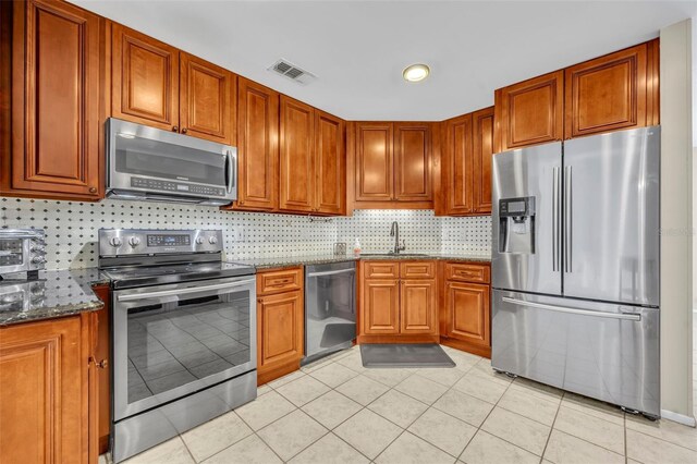 kitchen featuring stainless steel appliances, a sink, decorative backsplash, and dark stone counters