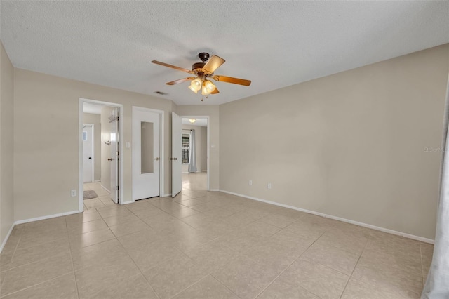 empty room with a ceiling fan, light tile patterned floors, baseboards, and a textured ceiling