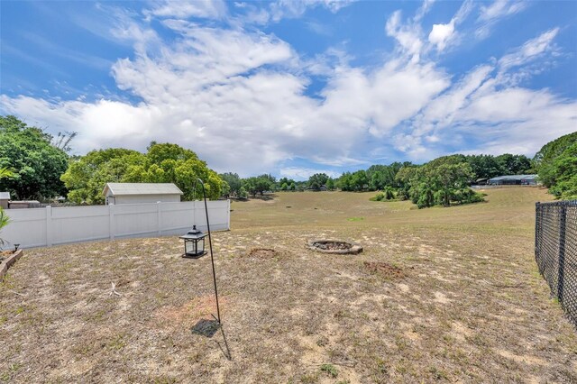 view of yard with fence, an outdoor fire pit, and view of scattered trees