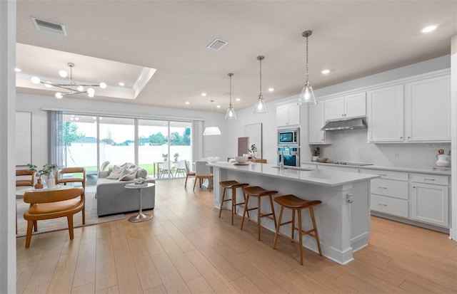 kitchen with stainless steel appliances, under cabinet range hood, open floor plan, light countertops, and a kitchen breakfast bar