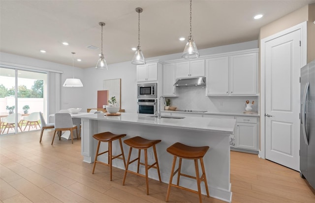 kitchen featuring stainless steel appliances, under cabinet range hood, light wood-style flooring, light countertops, and backsplash