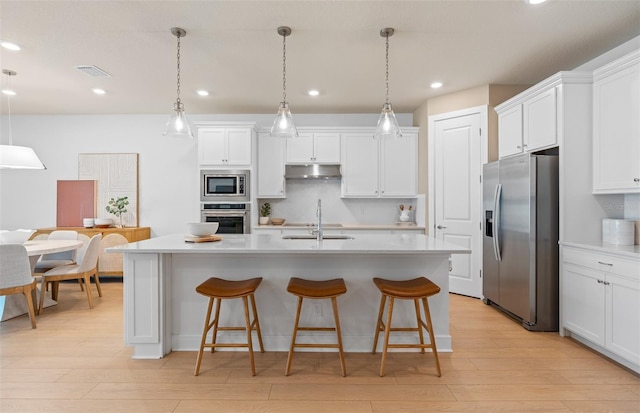 kitchen with stainless steel appliances, under cabinet range hood, a sink, light wood-style flooring, and recessed lighting