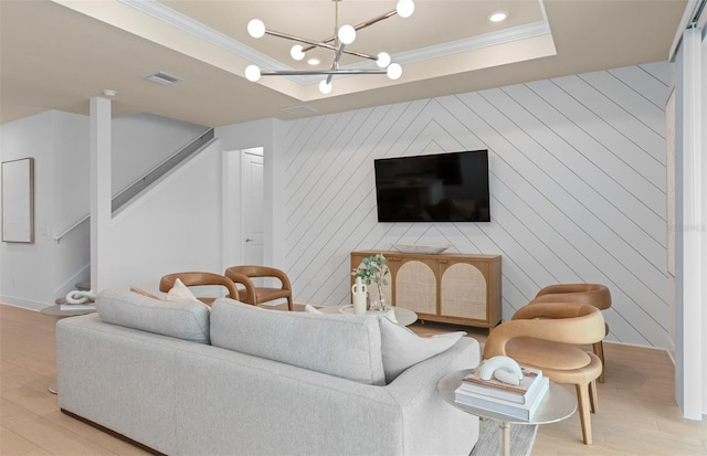 living area featuring crown molding, stairs, light wood-style floors, a chandelier, and a tray ceiling