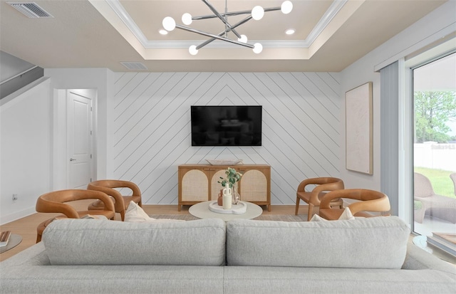 living area with wood finished floors, ornamental molding, a raised ceiling, baseboards, and a chandelier