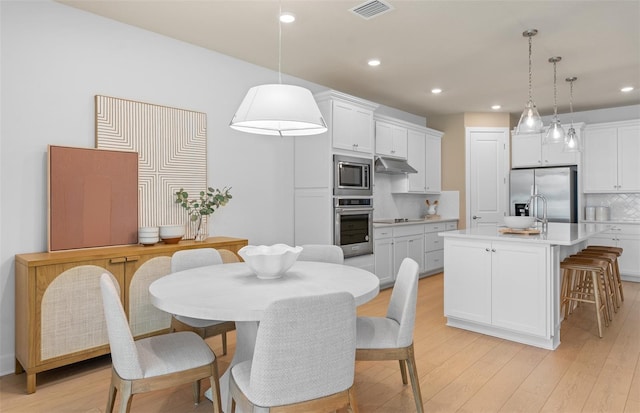 kitchen with appliances with stainless steel finishes, light wood-type flooring, decorative backsplash, under cabinet range hood, and recessed lighting