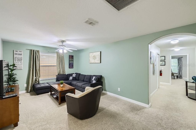 living area with arched walkways, light carpet, baseboards, and a ceiling fan