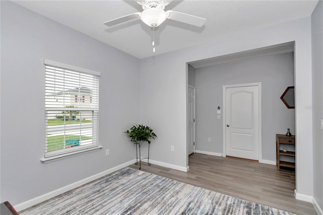 empty room with wood finished floors, a ceiling fan, and baseboards