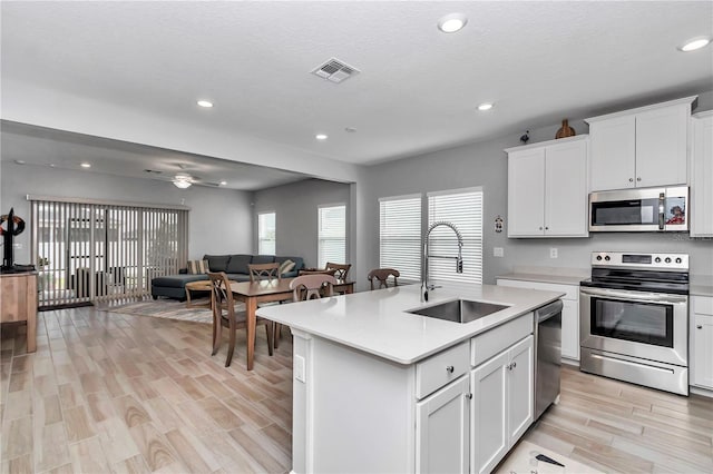 kitchen featuring appliances with stainless steel finishes, a sink, light countertops, open floor plan, and light wood-type flooring