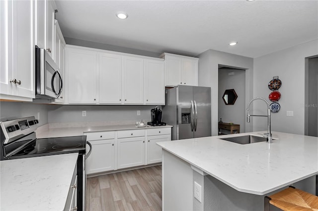 kitchen featuring appliances with stainless steel finishes, a sink, light wood-style flooring, white cabinetry, and recessed lighting