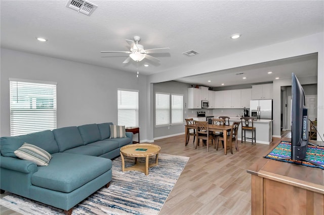 living room with healthy amount of natural light, a ceiling fan, light wood-style floors, baseboards, and recessed lighting
