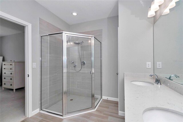 full bath with a shower stall, baseboards, wood finished floors, and double vanity