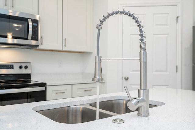 kitchen featuring white cabinets, stainless steel appliances, light stone counters, and a sink