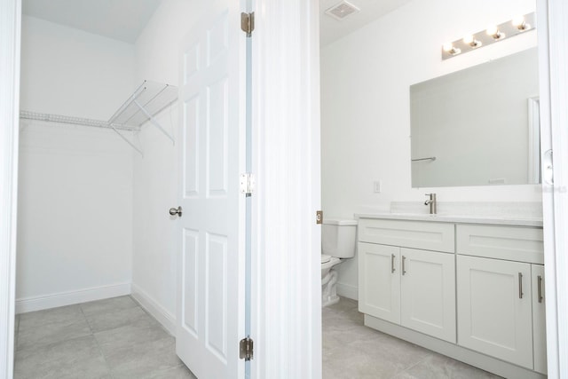 bathroom with toilet, vanity, visible vents, a spacious closet, and baseboards