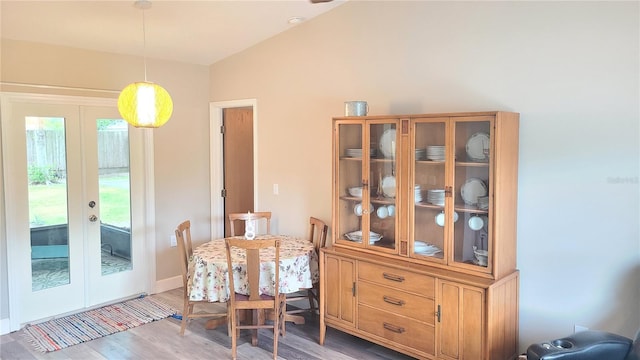 dining area featuring french doors, light wood-type flooring, lofted ceiling, and baseboards