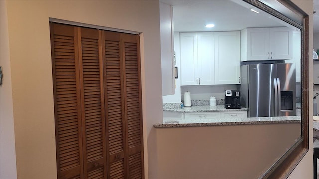 kitchen with stainless steel refrigerator with ice dispenser, white cabinets, and light stone countertops