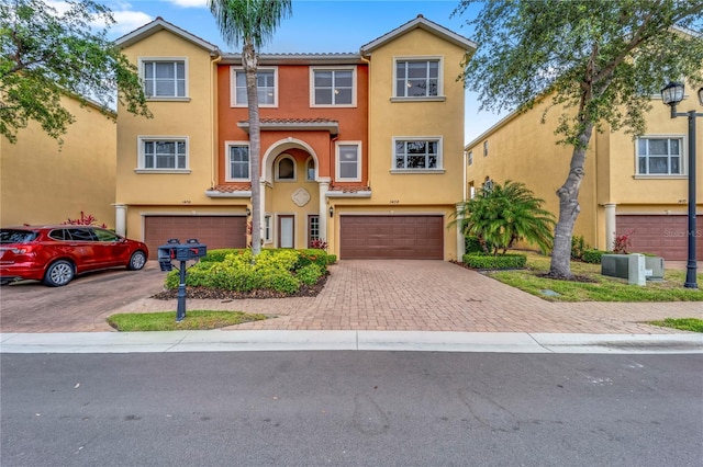 view of property with a garage, stucco siding, decorative driveway, and a tiled roof