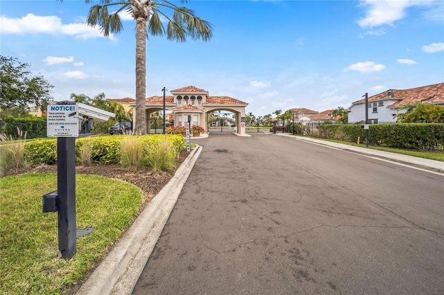 view of asphalt road with curbs, sidewalks, and a gated entry