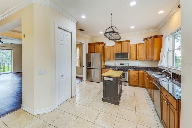 kitchen with appliances with stainless steel finishes, a sink, brown cabinetry, butcher block countertops, and a kitchen island