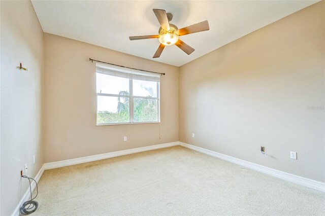 spare room featuring light colored carpet, ceiling fan, and baseboards