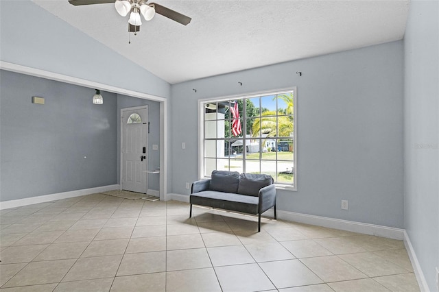 living area featuring ceiling fan, lofted ceiling, light tile patterned floors, baseboards, and a textured ceiling