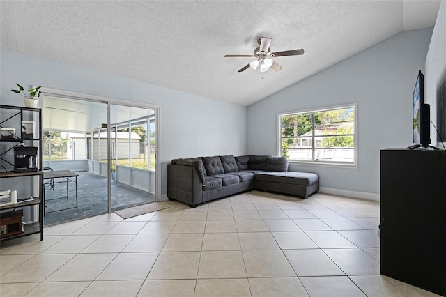 living room with lofted ceiling, ceiling fan, a textured ceiling, baseboards, and light tile patterned flooring