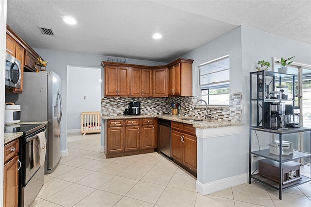 kitchen featuring appliances with stainless steel finishes, a sink, backsplash, brown cabinets, and light stone countertops