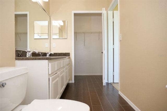 bathroom with toilet, vanity, and a walk in closet
